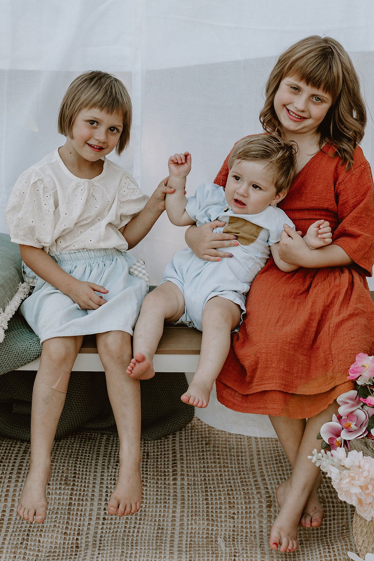 Emma and Sunny's three young children sitting playfully on a bench outdoors, representing the little adventurers behind the inspiration for the brand.