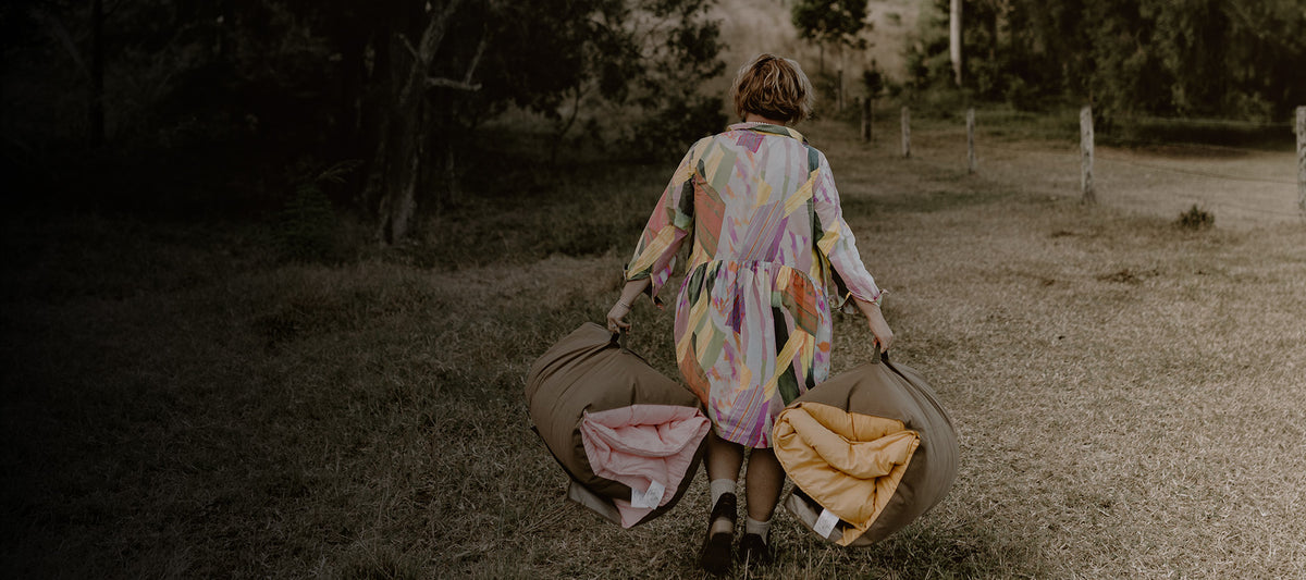 Cozie Dozie Co. founder Emma carrying two rolled Joey lounger covers in country canvas bags across a grass field in Central Queensland.