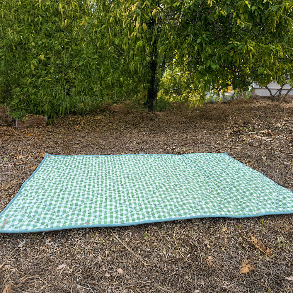 Quilted green gingham Co-mpanion Swag Mat with light blue trim laid flat on grass in an outdoor garden setting.