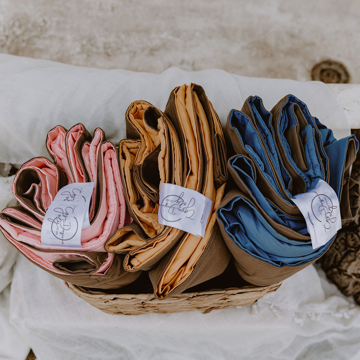 Rolled Cozie Dozie Co. Joey lounger covers in Quartz, Ochre, and BowerBird Blue neatly arranged in a basket with branded tags, highlighting small-batch Australian craftsmanship.