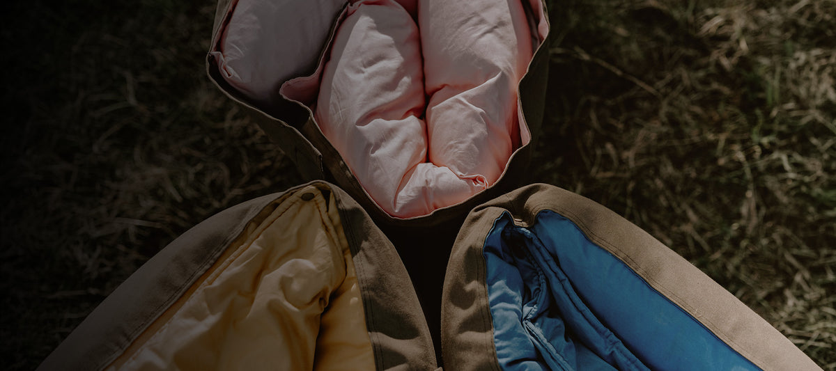 Close-up view of three rolled Cozie Dozie Co. Joey adventure lounger covers showing Quartz pink, Ochre yellow, and BowerBird Blue recycled linen linings with rugged canvas backings.