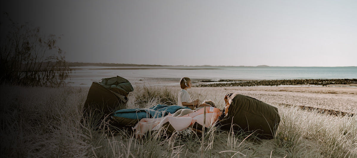 Children sitting on eco-friendly Cozie Dozie Co. Joey loungers made with recycled French linen and PUL canvas on a coastal beach in Central Queensland.