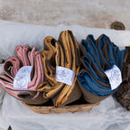 Top-down view of three neatly folded Cozie Dozie Co. Joey adventure loungers in Quartz pink, Ochre yellow, and BowerBird Blue placed inside a woven storage basket.
