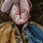 Top-down view of three rolled Joey adventure loungers in Quartz pink, Ochre yellow, and BowerBird Blue resting together on dry country grass.