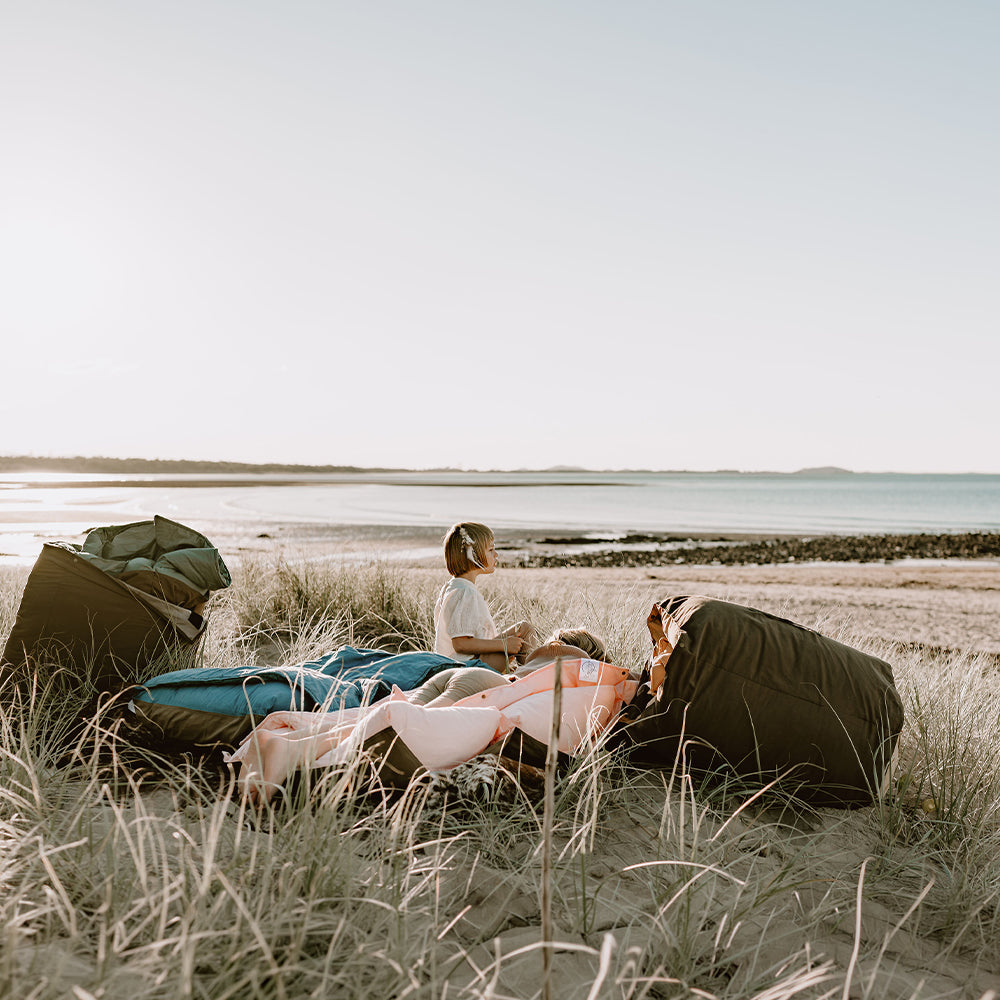 Children relaxing on Cozie Dozie Co. Joey adventure loungers in coastal sand dunes overlooking the beach and ocean in Central Queensland.