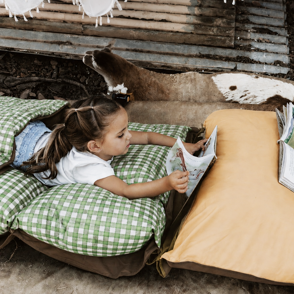 Child resting and reading on a Warrigal Greens green gingham Joey lounger alongside an Ochre yellow lounger in a rustic country barn setting.