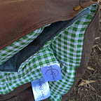 Close-up detail view of the Limited Edition Warrigal Greens Joey lounger rolled inside its canvas bag, highlighting the green gingham fabric, Cozie Dozie Joey branded tags, and bronze press stud.
