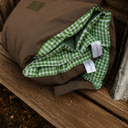Rolled Cozie Dozie Co. Limited Edition Warrigal Greens Joey lounger resting on a rustic wooden bench, showcasing the brown canvas backing and green gingham inner lining.