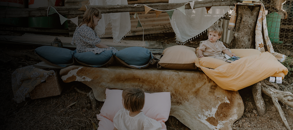 Children enjoying a country boho experience, lounging on Cozie Dozie Co. Joey adventure loungers in BowerBird Blue, Ochre, and Quartz at an outdoor play setup.