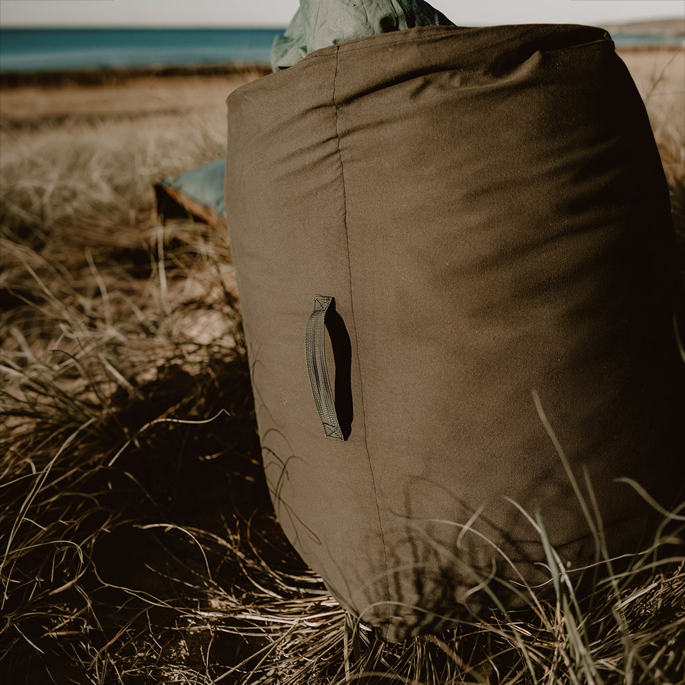 Close-up of a rolled Cozie Dozie Co. adventure lounger showing the durable canvas backing and stitched carrying handle in coastal beach grass.