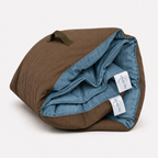 Rolled Cozie Dozie Co. The Buck modular adventure lounger cover in Sea Moss showing brown canvas backing and branded tags against a white background.